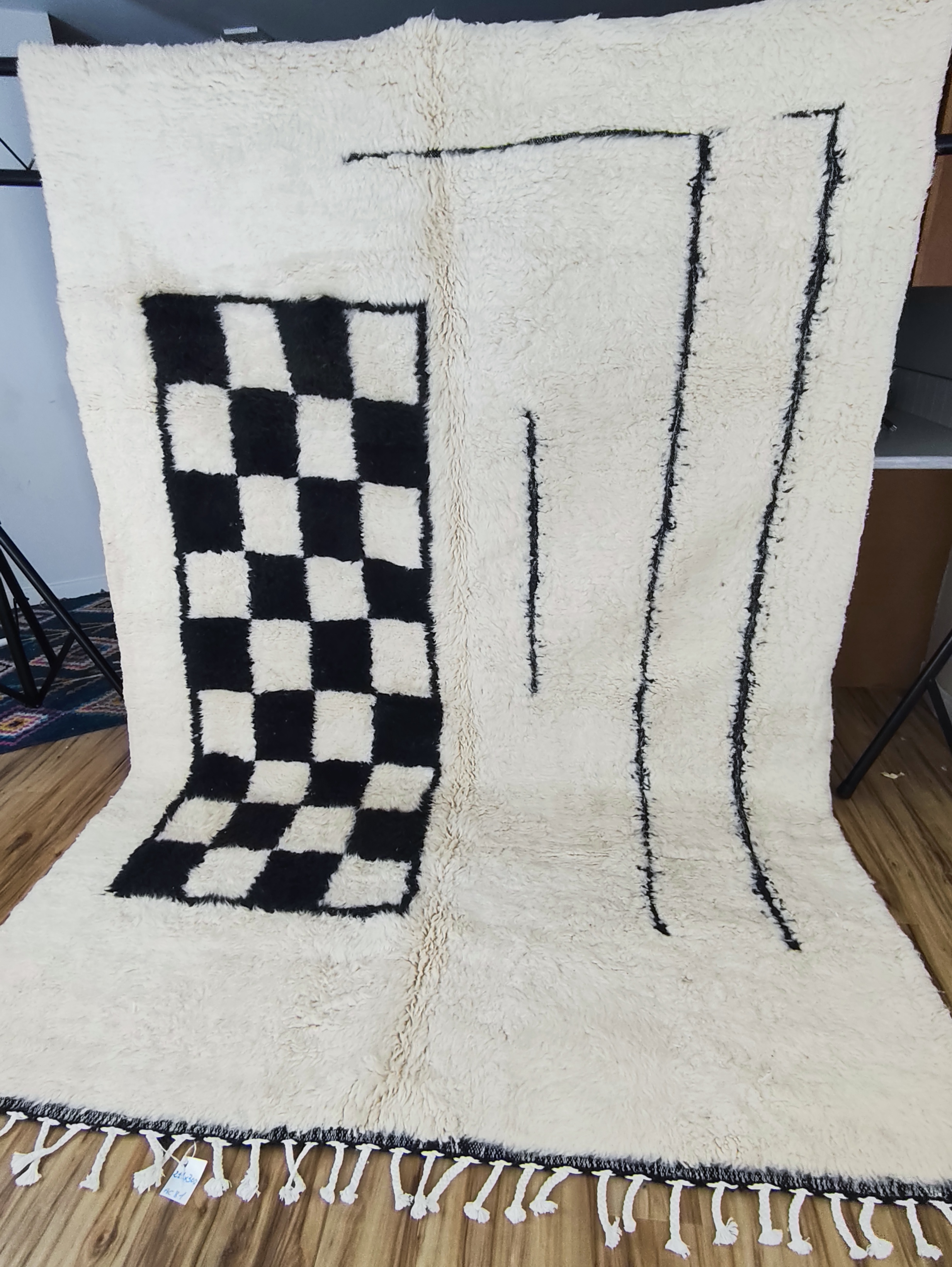 Black and white Moroccan rug with bold checkerboard field and hand-drawn line art composition, alternating fringe, hung in studio