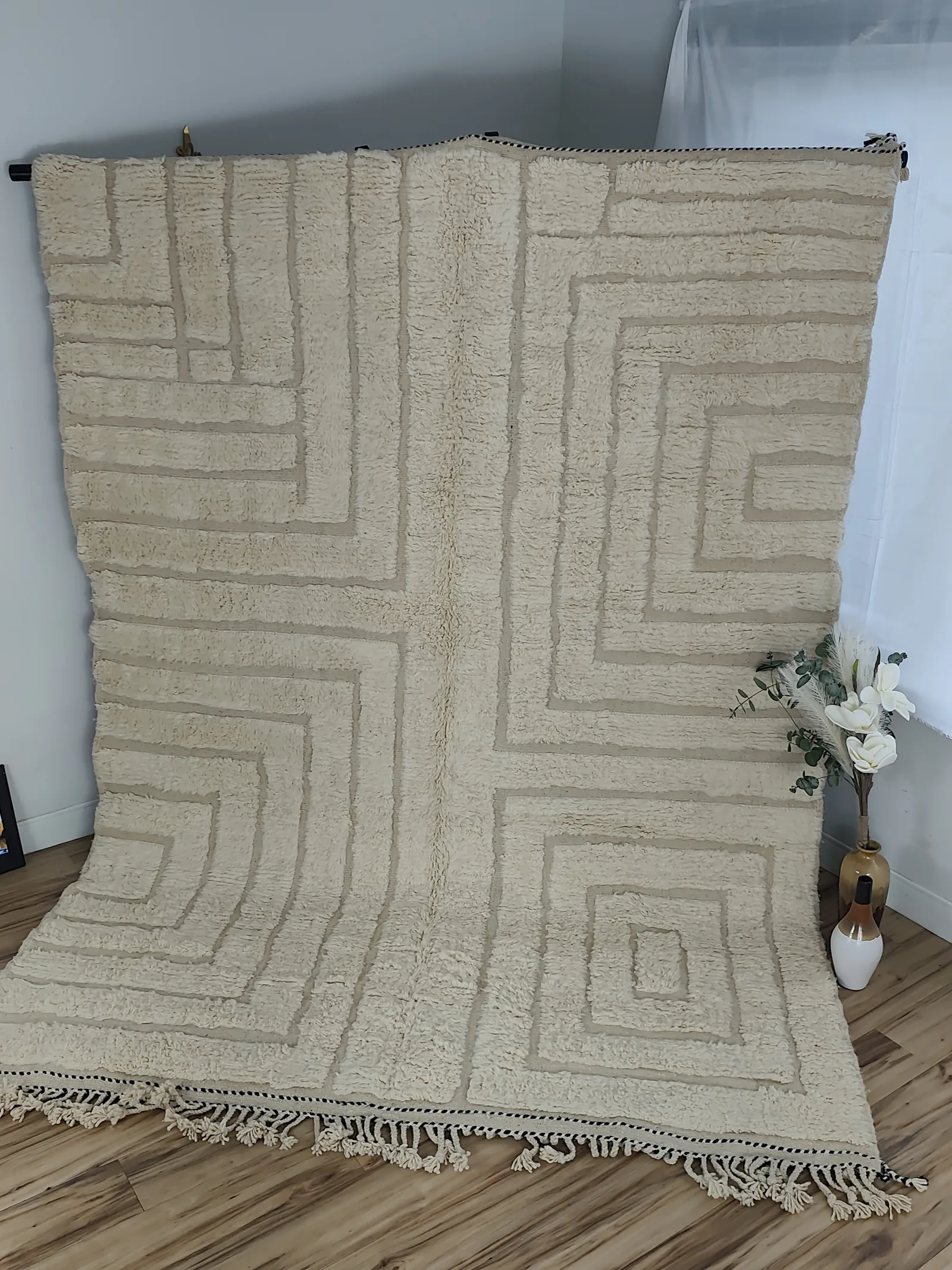 Latifa — hung from a rail beside a vase of flowers, the corner-flip reveals a natural linen flat-woven back, view 7 of 21
