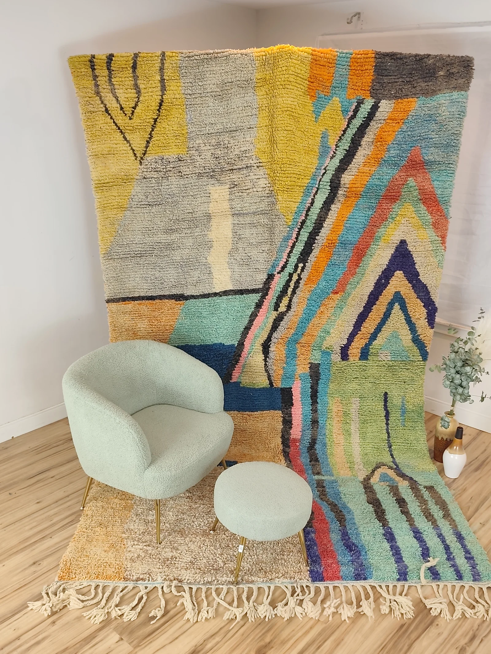 Soukaina — hung from a rail behind a sage boucle chair and stool, an abstract Boujaad in teal, blush and mustard, with bold diagonal bands cutting across a cream ground, view 1 of 20