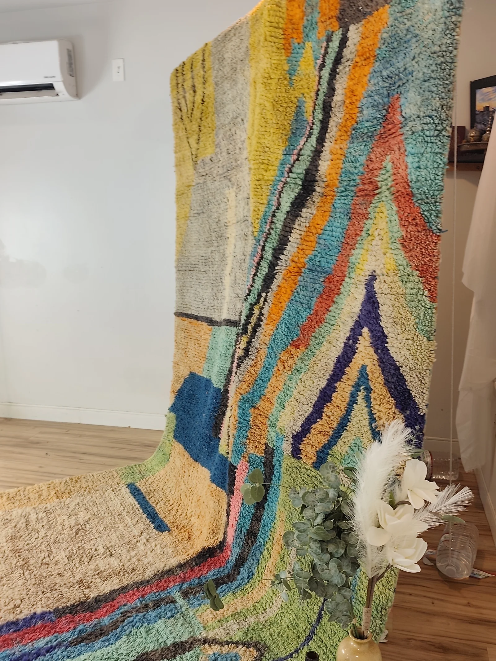 Soukaina — the hung rug cascading onto the floor beside flowers, Boujaad Moroccan rug from Morocco, 323 × 178 cm, view 12 of 20
