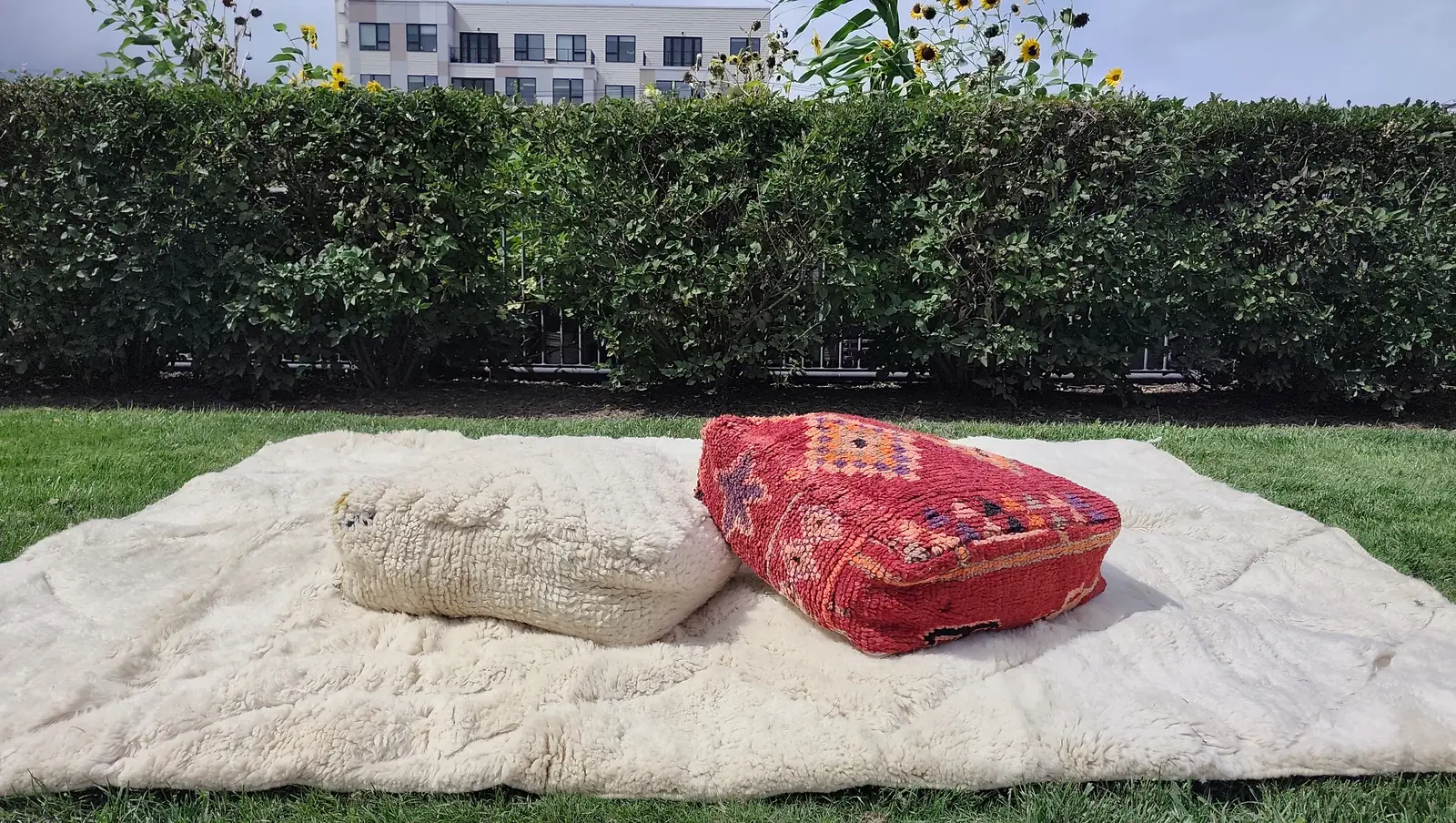 Tafsut — seen across its width on the grass, two poufs at one end, the ivory field reading almost white against the green, view 3 of 18