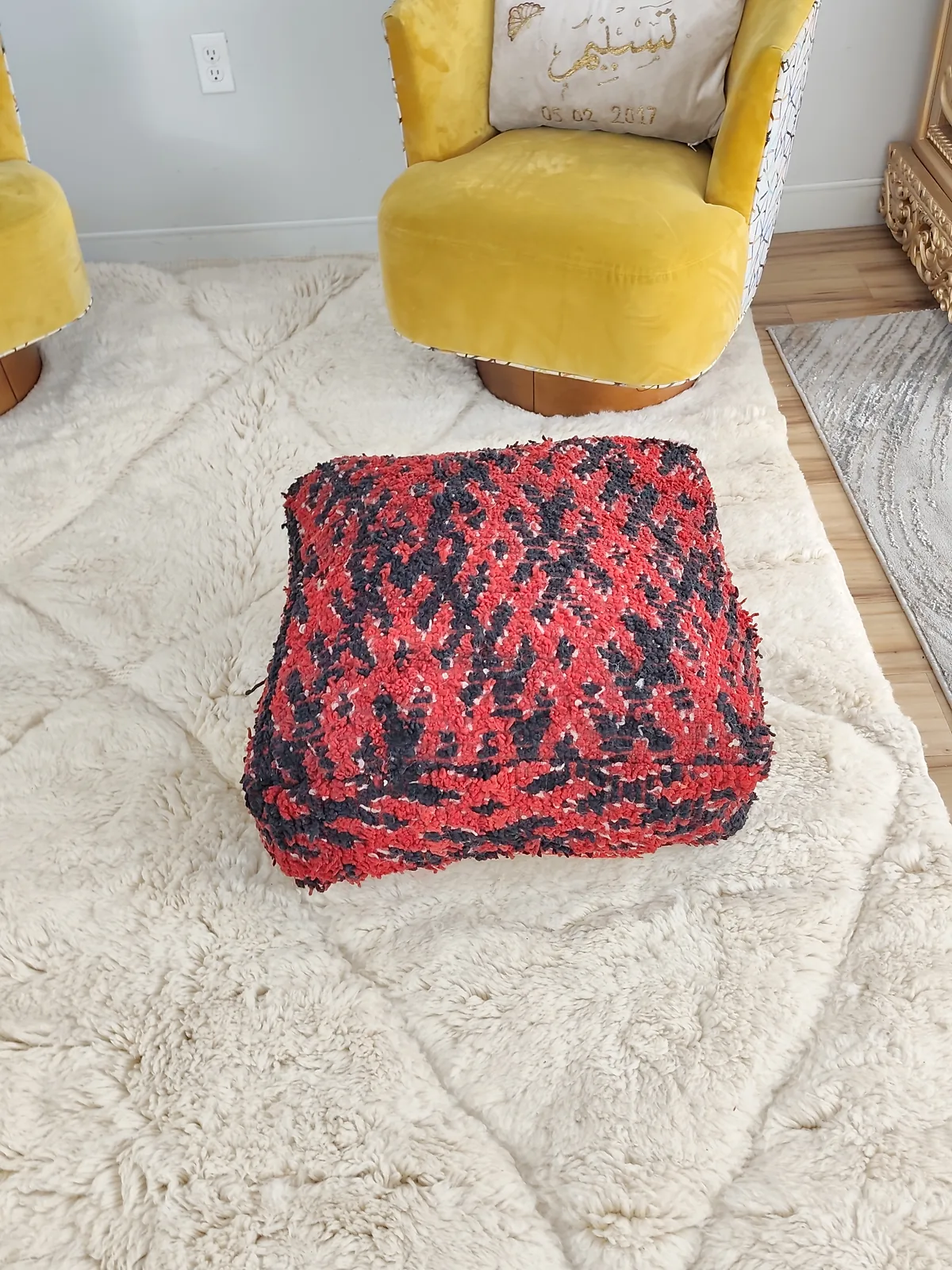 Kahina — red & black boucherouite pouf, styled beside a mustard armchair, view 6 of 7